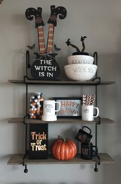 halloween decorations on shelves in the corner of a room with two mugs and other items