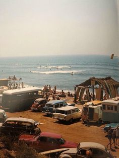 many cars are parked on the beach by the ocean and people in the water behind them