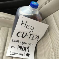 a bottle of water sitting on top of a car seat next to a sign that says hey cutta will you go to prom with me?