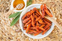 a bowl filled with carrots next to a wooden spoon on top of a woven mat