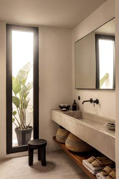 a bathroom with a large mirror, sink and stool next to a plant in the corner