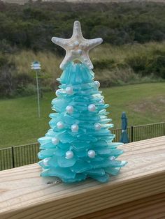 a blue christmas tree made out of plastic bottles and seashells on a deck