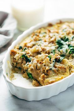 a casserole dish with spinach and cheese in it next to a glass of milk