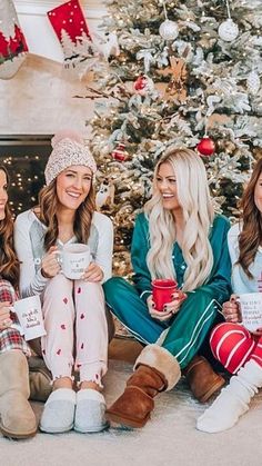 three women sitting in front of a christmas tree holding mugs