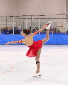 a female figure skating on an ice rink wearing a red dress and holding her leg in the air