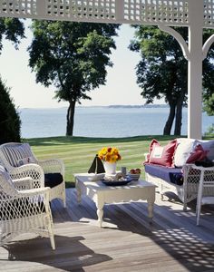 an outdoor living area with white wicker furniture and water in the backgroud