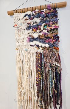 a wall hanging made out of yarn and other items on a wooden stick with a white background