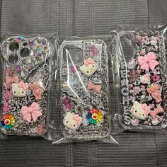 three cell phones with hello kitty designs on them in plastic cases, one is pink and the other is silver