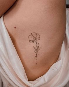 a woman's stomach with a single flower tattoo on the side and behind her belly