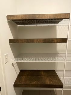 empty shelves in the corner of a room with white walls and brown wood flooring