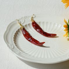 two red chili peppers on a white plate next to yellow flowers and sunflowers