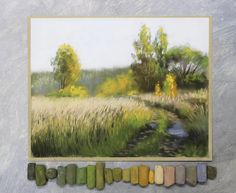 pastel pencils are arranged in front of an image of a field and stream