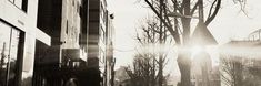 black and white photograph of the sun shining down on a city street with tall buildings