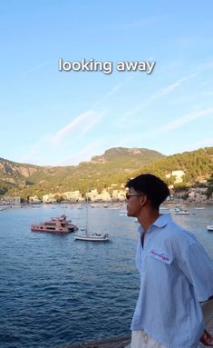 a man standing on the edge of a cliff looking out at boats in the water