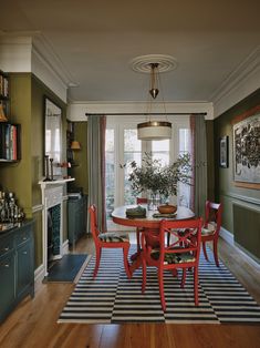 a dining room with green walls and wooden floors, red chairs around a round table