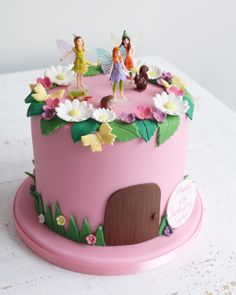 a pink cake with tinkerbells on top and flowers around the edges, sitting on a white table