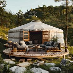 a yurt with couches and chairs in the grass next to rocks, trees and bushes