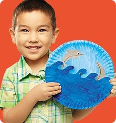 a young boy holding up a paper plate with an image of a dolphin on it