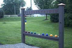 a sign that has balls on it in front of some trees and grass with a fence behind it