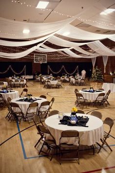 tables and chairs are set up in the center of an indoor banquet hall with white draping