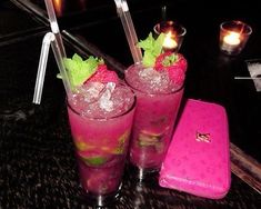 two glasses filled with ice and strawberries next to a pink wallet on a table