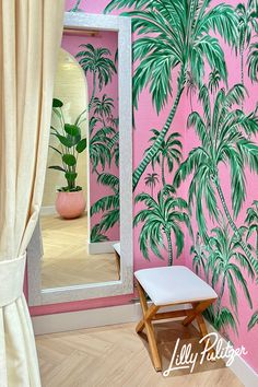 a palm tree painted on a pink wall next to a white chair and large mirror