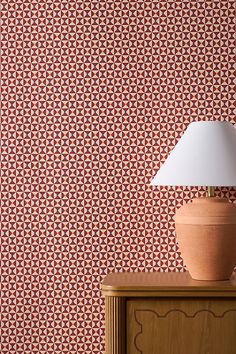 a lamp sitting on top of a wooden dresser next to a wallpapered wall