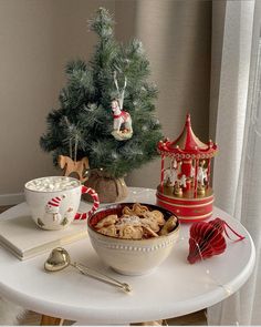 a white table topped with a bowl of cereal next to a christmas tree and other decorations