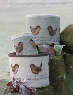 three fabric pots with birds on them sitting on a stone wall next to some leaves