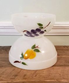 a white vase with fruit painted on it sitting on a wooden table next to a wall