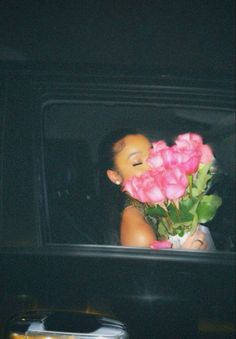 a woman is holding pink roses in the back of a car with her eyes closed