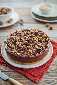 a chocolate cake with nuts on top sitting on a plate next to a knife and fork