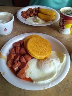 two plates with breakfast foods on them sitting on a table next to cups and coffee