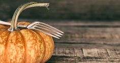 an orange pumpkin with a fork sticking out of it's side sitting on a wooden table