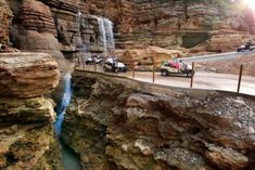 several people riding on four wheelers in front of a waterfall with cars driving down it