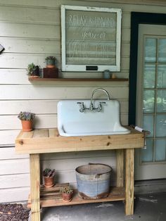 a white sink sitting on top of a wooden table next to a window and potted plants