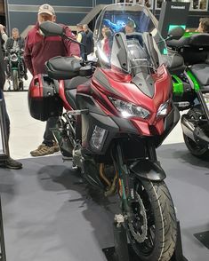 a red motorcycle parked on top of a gray floor next to other motorcycles and people