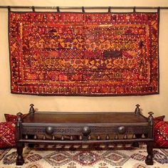 an antique bench is sitting in front of a large rug on the wall behind it