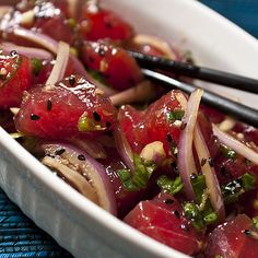 a white bowl filled with watermelon, onions and chopsticks on top of a blue cloth