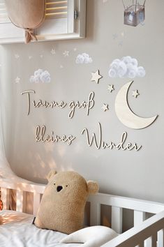 a teddy bear sitting on top of a bed next to a wall with words and clouds