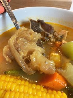 a bowl of soup with meat, vegetables and corn on the cob