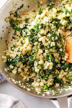 a pan filled with rice and spinach next to a wooden spoon