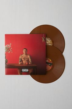 two brown vinyl records sitting next to each other on top of a white table with a red wall in the background