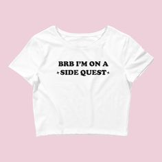 The "BRB On a Side Quest" Women's Crop Baby Tee is a stylish and unique t-shirt designed for music festival-goers and fans of the Y2K rave culture. This crop top combines a playful design with a trippy aesthetic, making it a standout choice for those seeking an eye-catching and unconventional look. With its cropped design, this tee is perfect for pairing with high-waisted bottoms like skirts, shorts, or jeans, allowing you to create a trendy and fashionable outfit. The "BRB On a Side Quest" grap Fitted Rave T-shirt For Streetwear, Summer Graphic Tee With Band Logo, Punk Style Short Sleeve Tops For Music Festival, Fitted Text Print Top For Concert, Unisex Tops For Summer Music Festival, White Letter Print Tops For Music Festivals, Band Merch Crew Neck Tops For Music Festival, Crew Neck Top With Text Print For Music Festivals, Crew Neck Text Print Top For Music Festivals