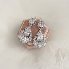 a pair of diamond earrings sitting on top of a pink velvet ring box with white lace