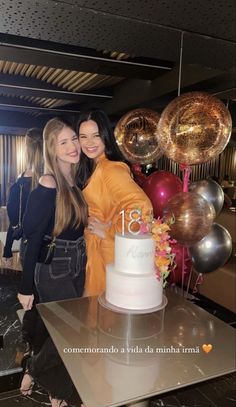 two women standing next to each other in front of a cake