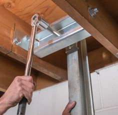 a person holding a wrench under a metal beam