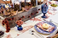 the table is set with plates, silverware and pumpkins in glass vases