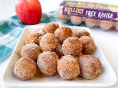 some sugared donuts are on a plate next to an apple and carton of eggs