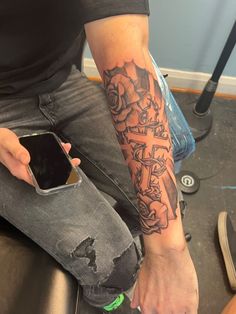 a person with a tattoo on their arm holding a cell phone and sitting down in a room